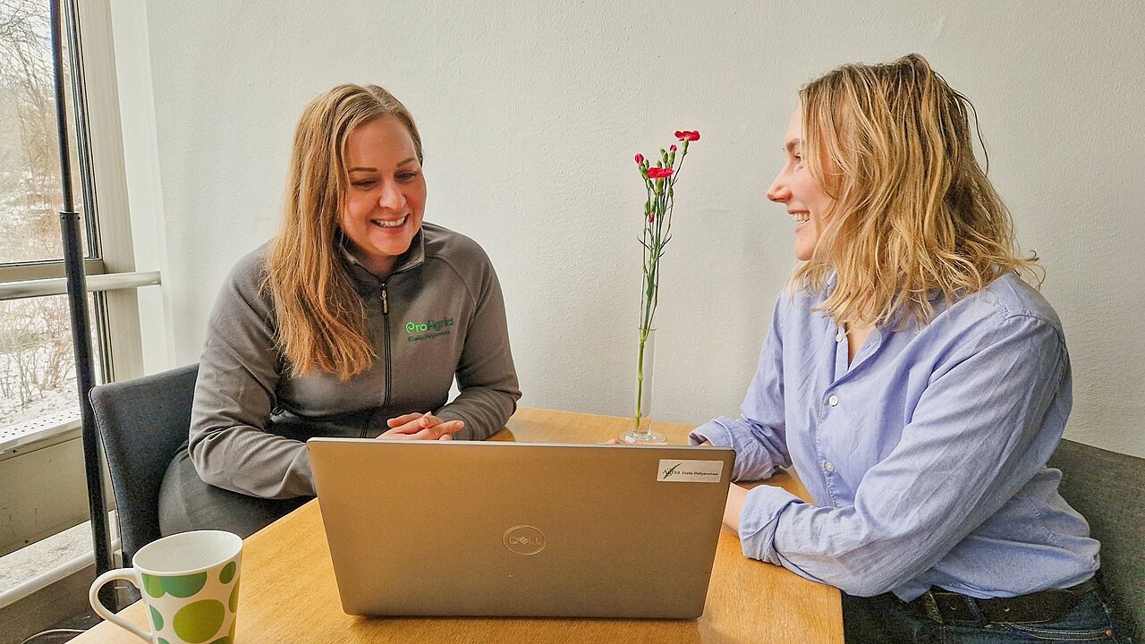 Kaksi henkiloa tyoskentelee poydan aaressa talvimaiseman aarella kannettava tietokone kukkia ja kahvimuki