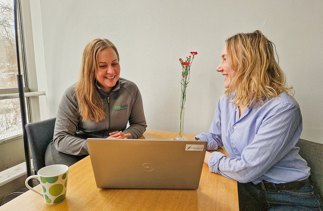 Kaksi henkiloa tyoskentelee poydan aaressa talvimaiseman aarella kannettava tietokone kukkia ja kahvimuki